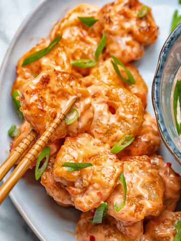Close up shot of bang bang shrimp being picked up from a plate with chop sticks