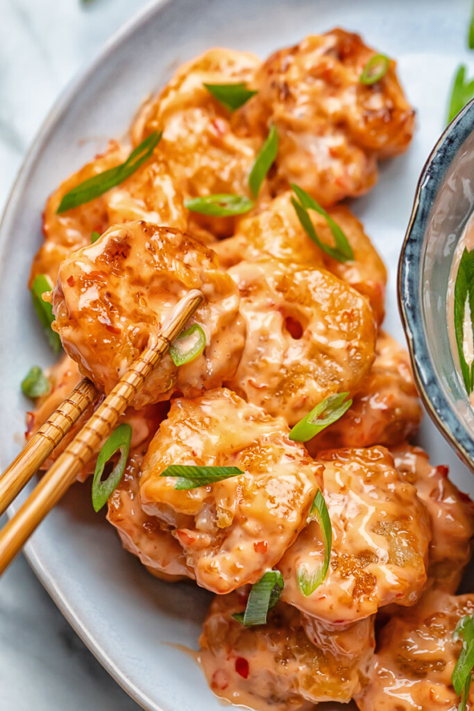 Close up shot of bang bang shrimp being picked up from a plate with chop sticks