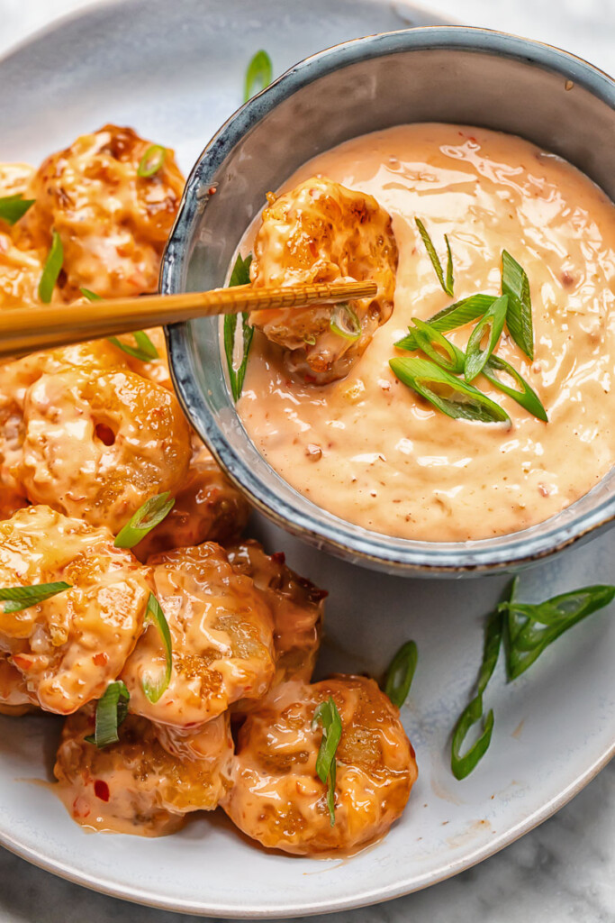 Close up shot of bang bang shrimp being dipped in spice mayo