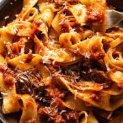 Close up shot of short rib ragu on a plate topped with grated Parmesan