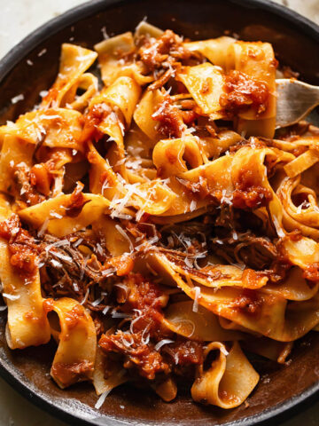 Close up shot of short rib ragu on a plate topped with grated Parmesan