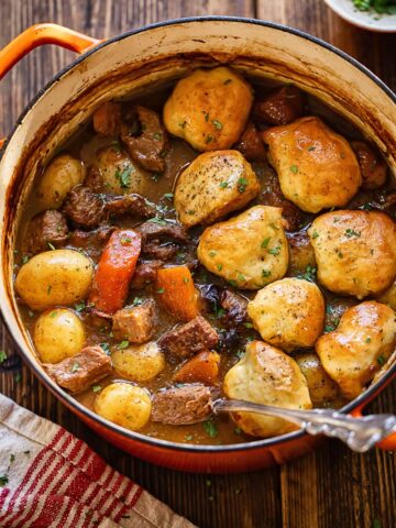 Top down shot of beeft stew and dumplings in a large pot with a serving spoon