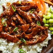Close up shot of beef teriyaki on a bed of rice with sliced carrot and green onions