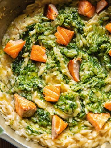 Close up shot of kale pesto orzo in a pan with salmon pieces