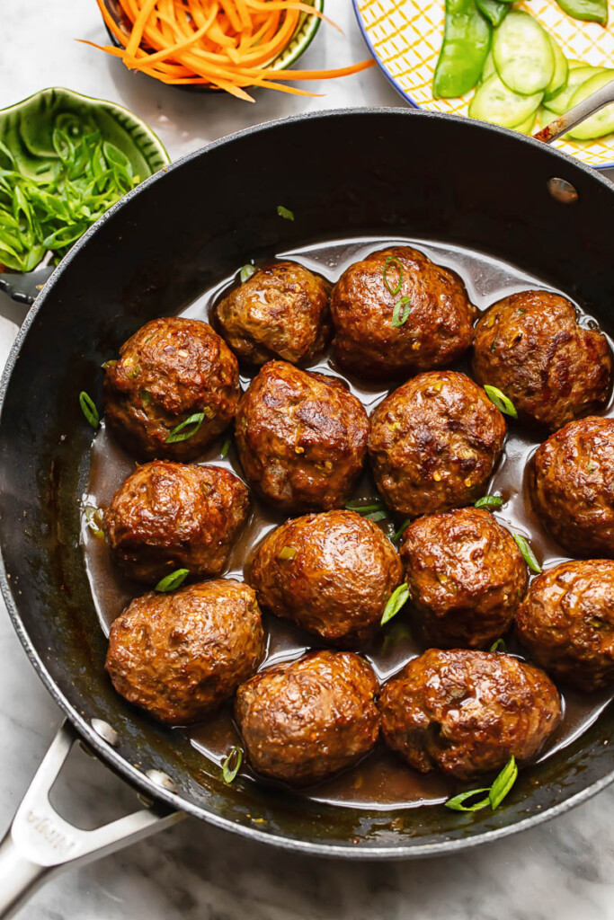 Top down shot of teriyaki meatballs in a wide pan topped with spring onions