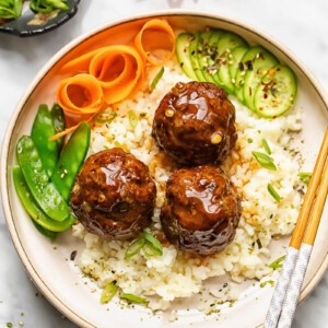 Close up shot of teriyaki meatballs with rice in a bowl with veg and chopsticks