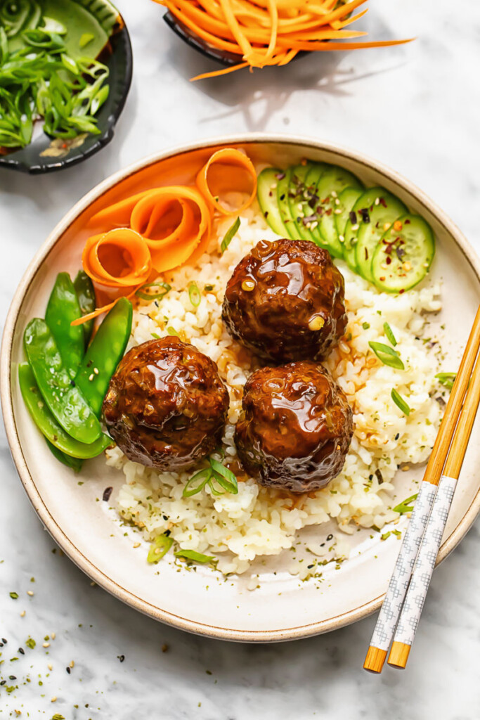 Close up shot of teriyaki meatballs with rice in a bowl with veg and chopsticks