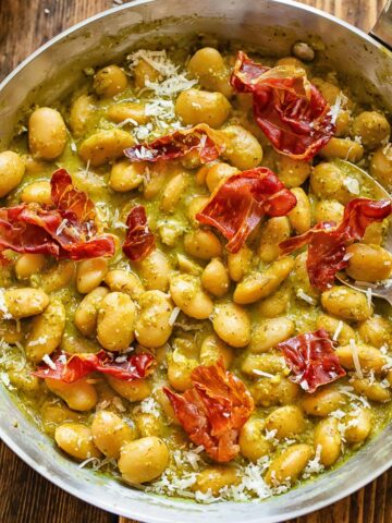 Top down shot of butter beans in a pan with creamy basil pesto sauce