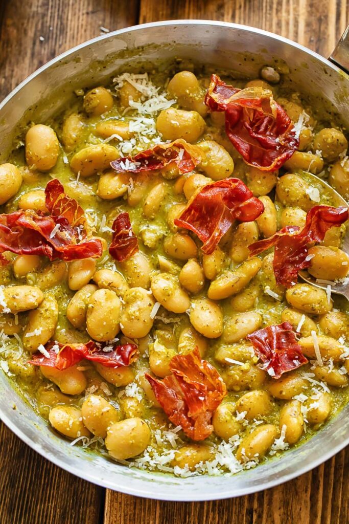 Top down shot of butter beans in a pan with creamy basil pesto sauce