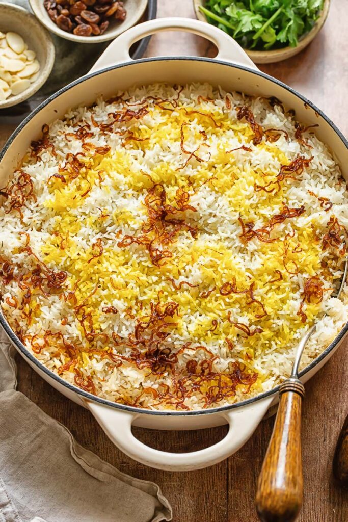 Top down shot of rice in a pan topped with spices, onions and almonds for chicken biriyani