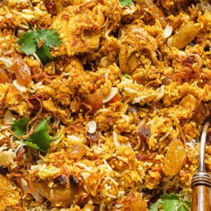 Top down shot of chicken biriyani in a pan with roasted almonds and fresh parsley garnish
