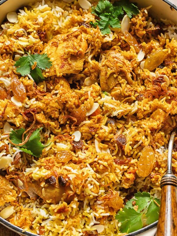 Top down shot of chicken biriyani in a pan with roasted almonds and fresh parsley garnish