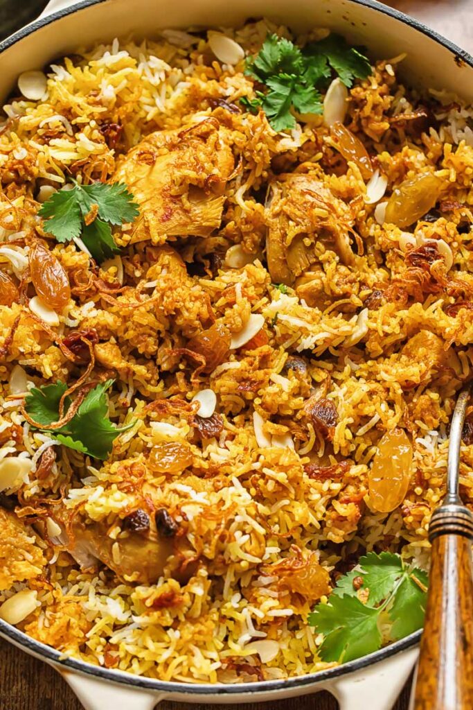 Top down shot of chicken biriyani in a pan with roasted almonds and fresh parsley garnish