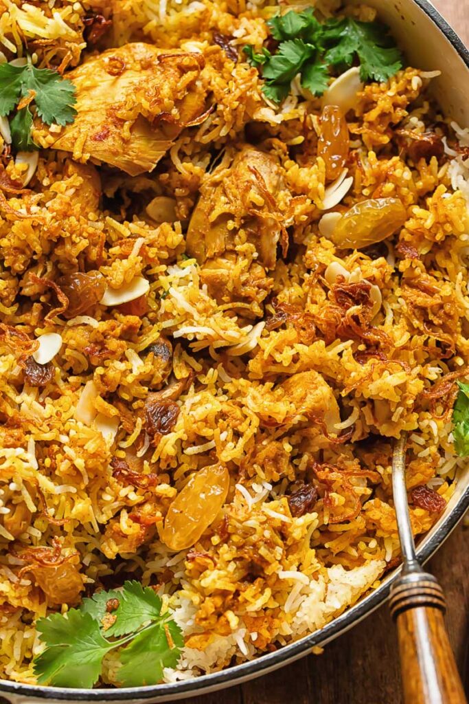 Close up shot of chicken biriyani in a pan with a serving spoon