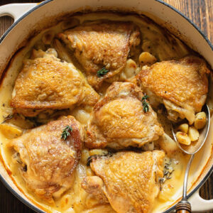 Top down shot of chicken with 40 cloves of garlic in a large wide pan