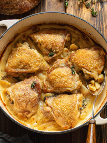 Top down shot of chicken with 40 cloves of garlic in a large wide pan
