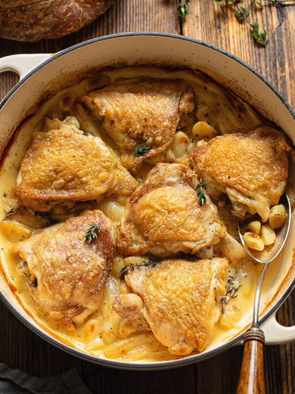 Top down shot of chicken with 40 cloves of garlic in a large wide pan