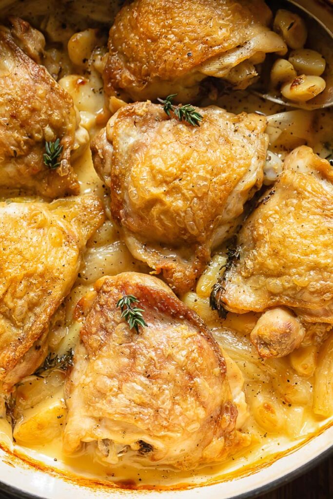 Close up shot of chicken thighs in a pan topped with rosemary garnish