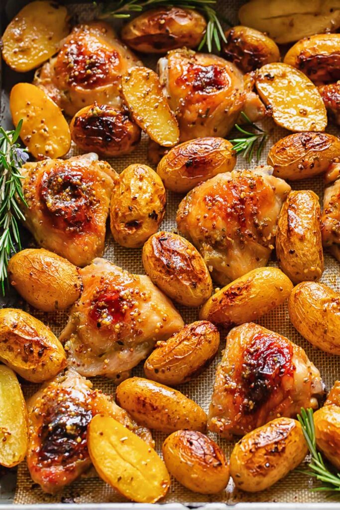 Top down shot of honey mustard chicken thighs in a baking tray with potatoes