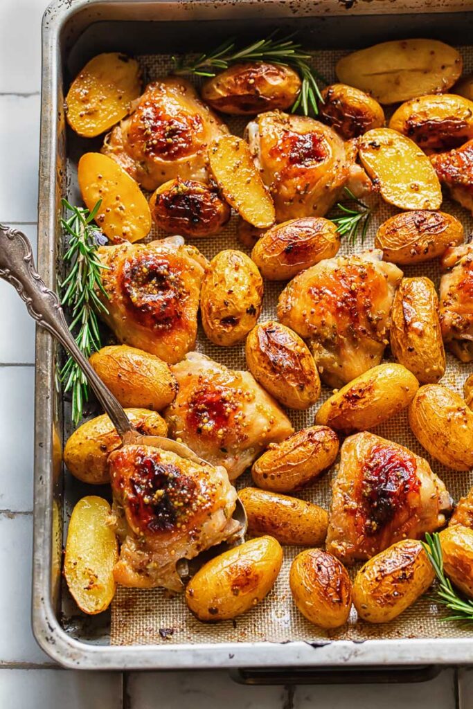 Top down shot of honey mustard chicken thighs with a serving spoon in a baking tray