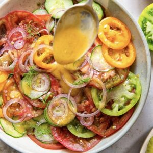 close up of tomato and cucumber salad with spoon adding vinaigrette