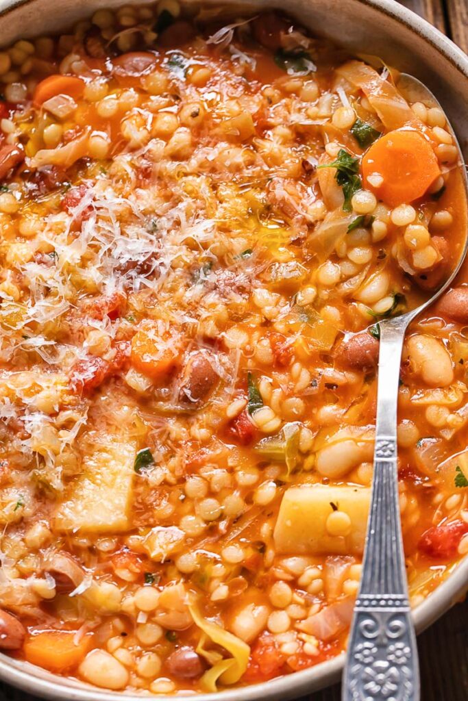 Close up shot of spoon scooping Sardinian minestrone topped with Parmesan out of a pot