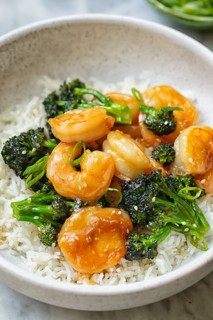 Close up shot of shrimp and broccoli stir fry on top of a bowl of rice