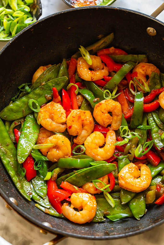 Top down shot of shrimp stir fry in a pan with veg topped with spring onions