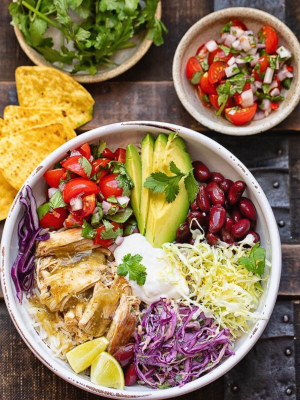 Top down shot of chicken and rice burrito bowls next to fresh veg and salsa toppings