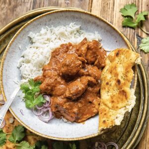 bowl of basmati rice with rogan josh curry poured over top and a piece of naan