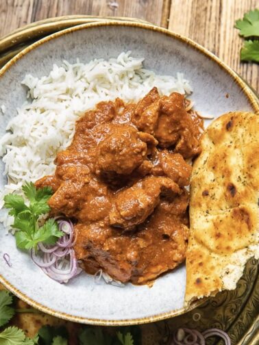 bowl of basmati rice with rogan josh curry poured over top and a piece of naan
