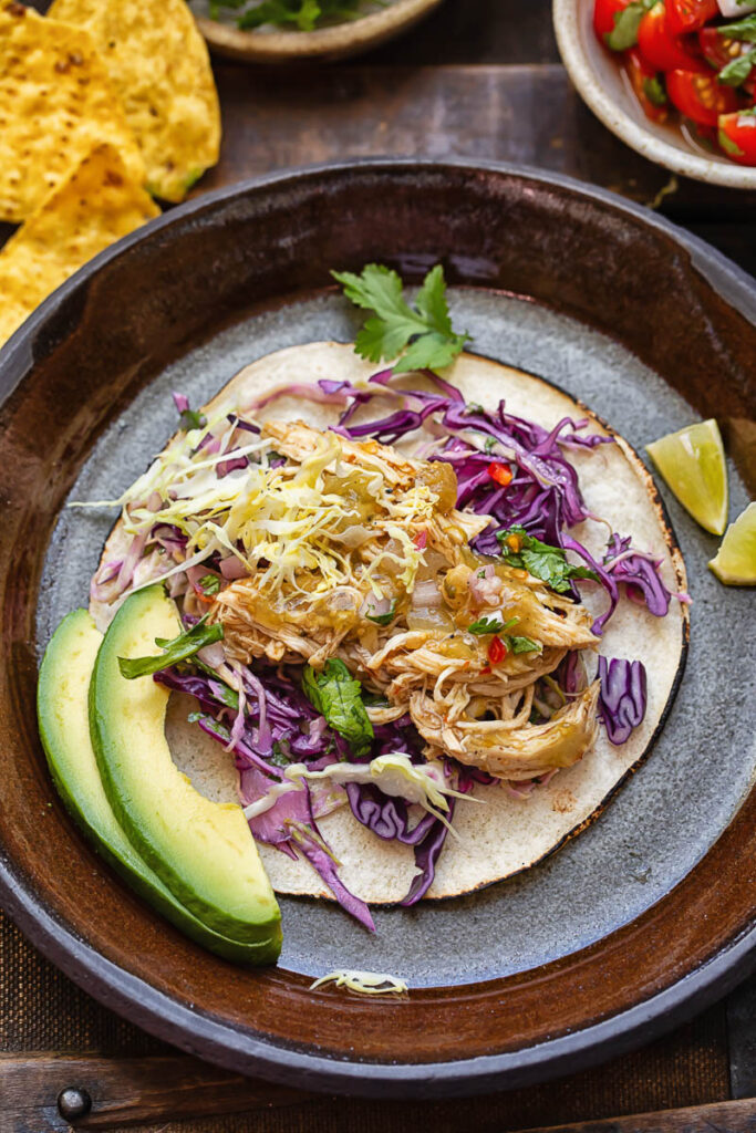Top down shot of salsa verde chicken taco with slaw and avocado on a plate
