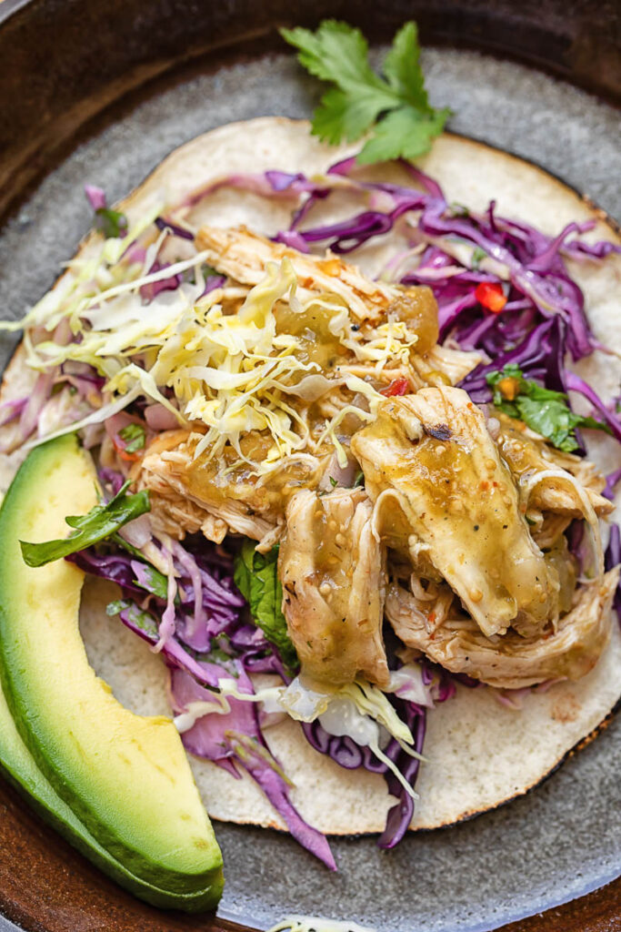 Top down shot of a taco on a plate with salsa verde chicken and fresh veg