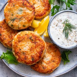 Top down shot of salmon cakes on a plate with a bowl of chive and garlic sauce