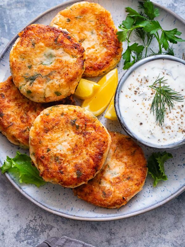 Top down shot of salmon cakes on a plate with a bowl of chive and garlic sauce