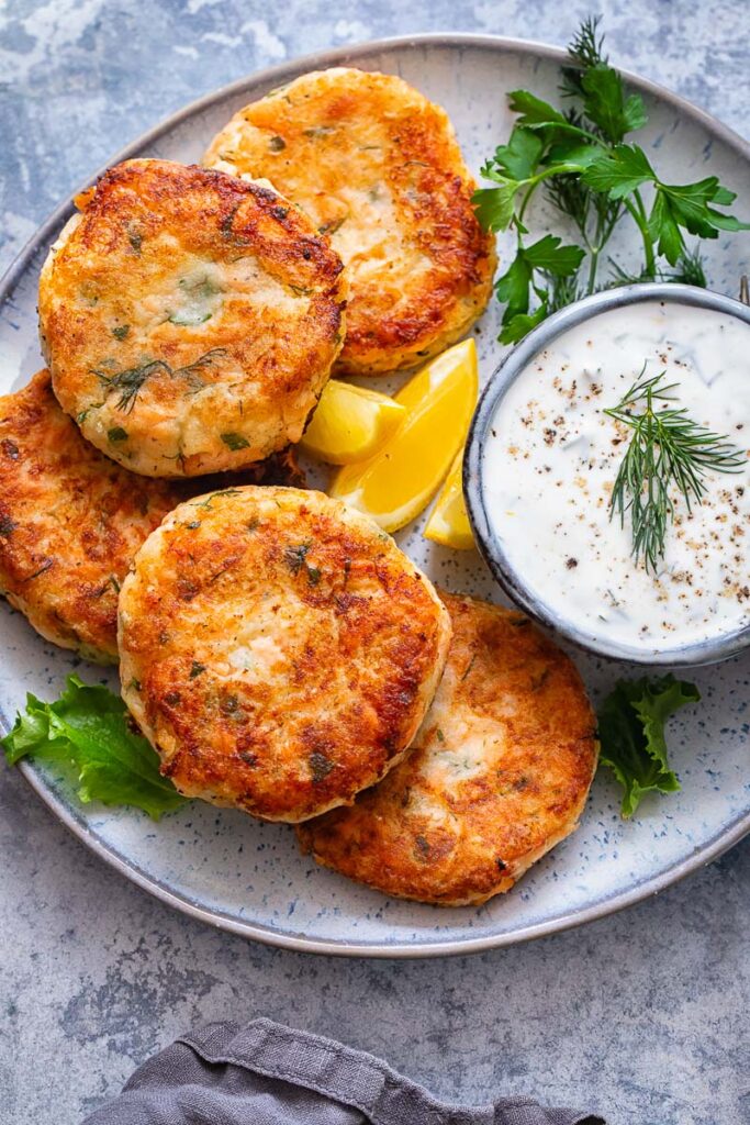 Top down shot of salmon cakes on a plate with a bowl of chive and garlic sauce