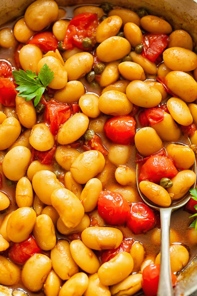 Close up shot of butter beans and tomato sauce topped with fresh basil with a spoon