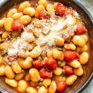 Top down shot of butter beans with cherry tomato sauce in a pan