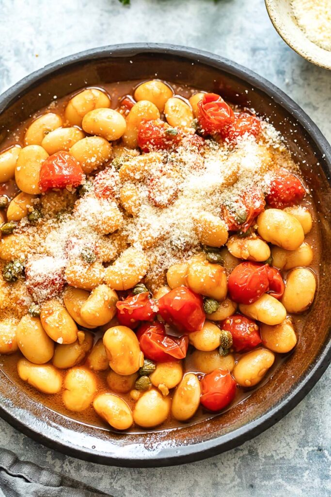 Top down shot of butter beans with cherry tomato sauce in a pan