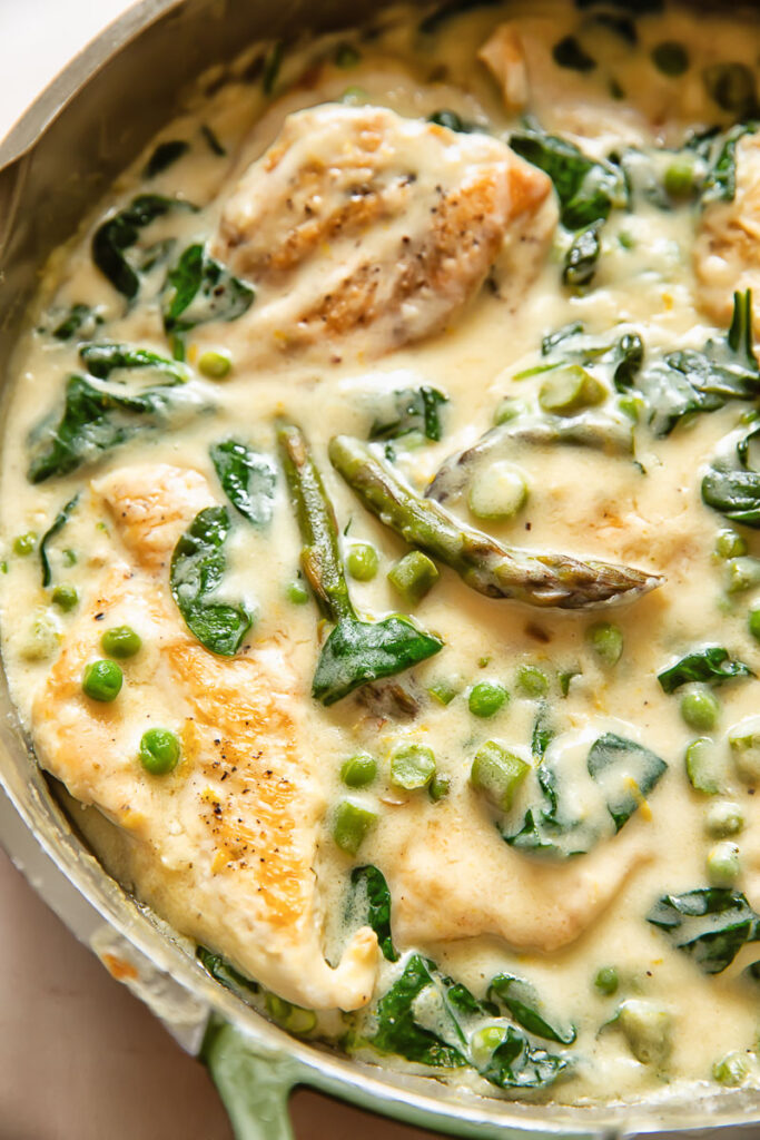 Close up shot of chicken primavera in cream sauce with peas and asparagus