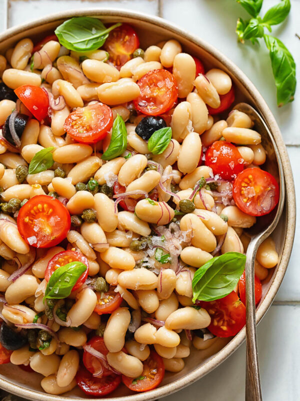 Top down shot of white bean salad in a serving bowl with basil garnish