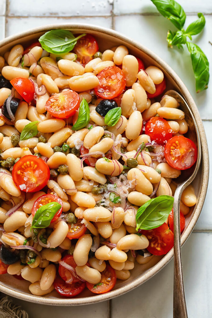 Top down shot of white bean salad in a serving bowl with basil garnish