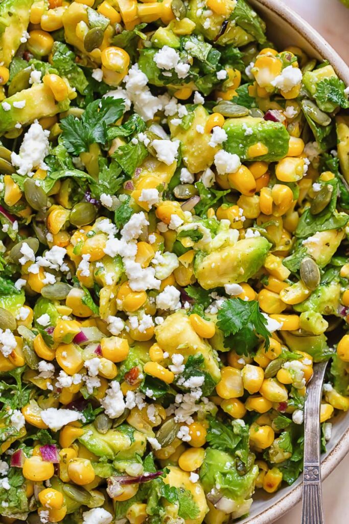 Close up of avocado corn salad topped with white cheese and cilantro