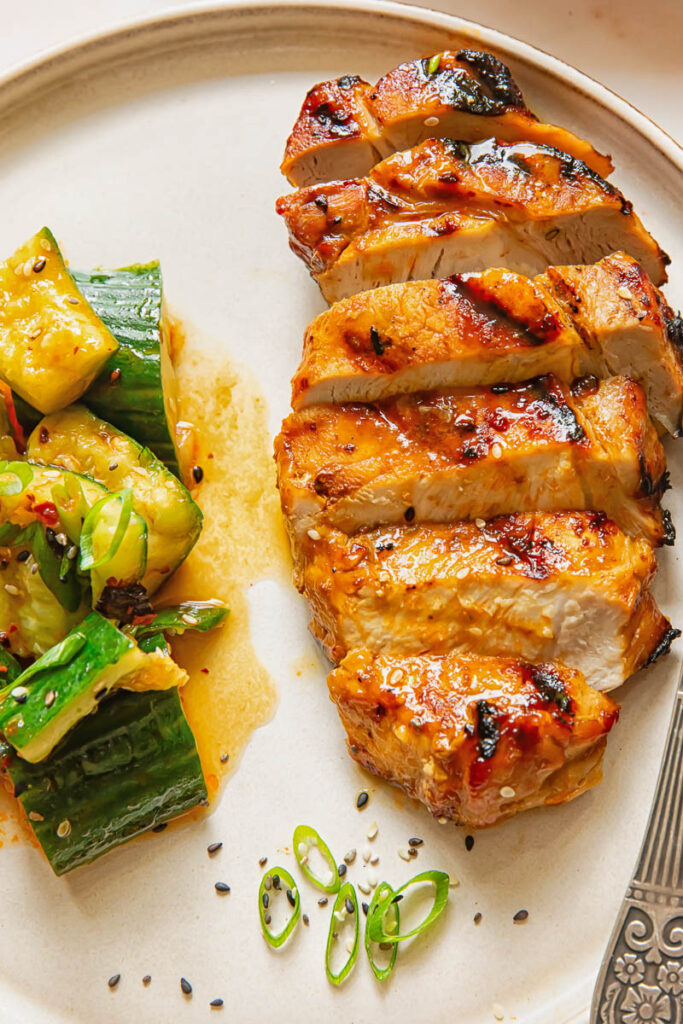 Sliced teriyaki pork chop next to a cucumber salad