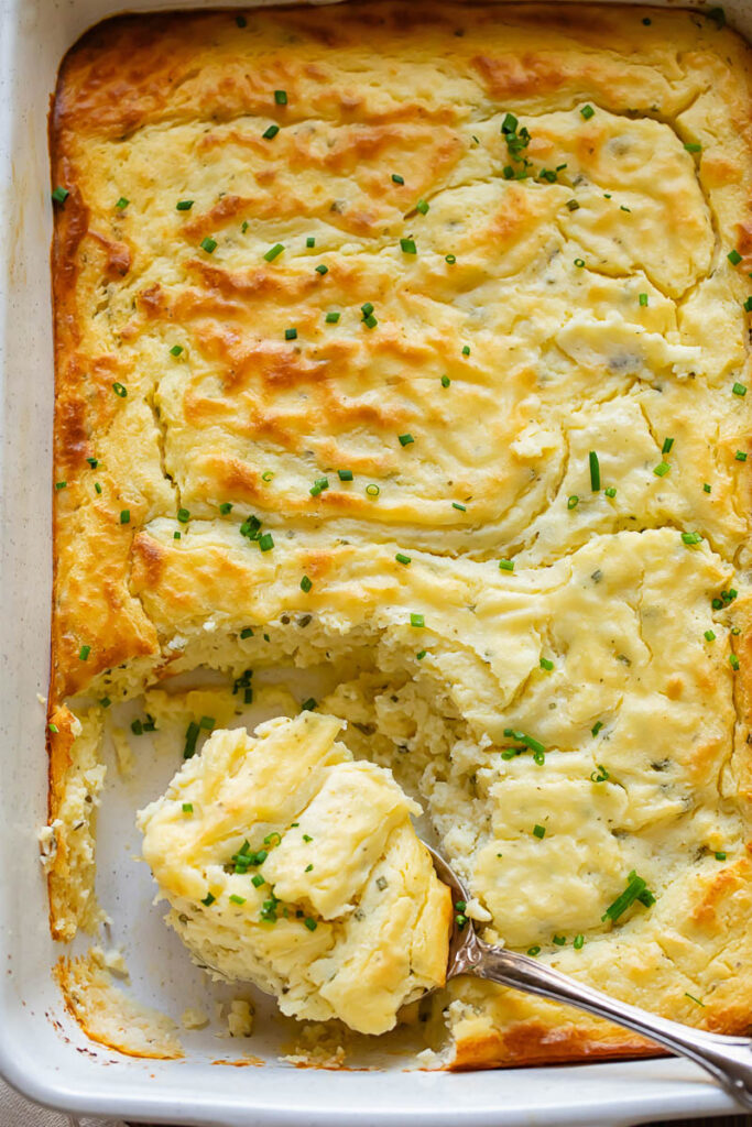 top down of a casserole dish with potato soufflé, with a serving spoon removing a portion