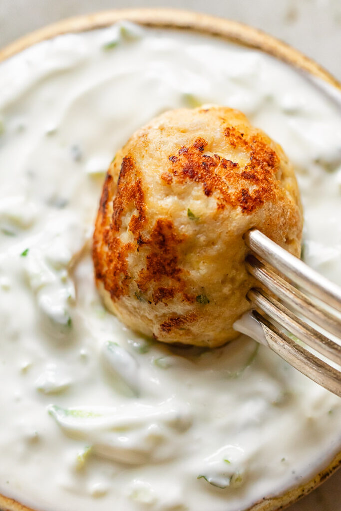 Close up of chicken meatball being dipped in tzatziki