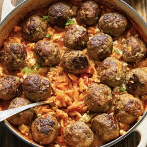 pan filled with orzo in a red sauce and topped with several meatballs