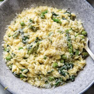 shallow bowl with orzo and vegetables topped with shredded parmesan cheese