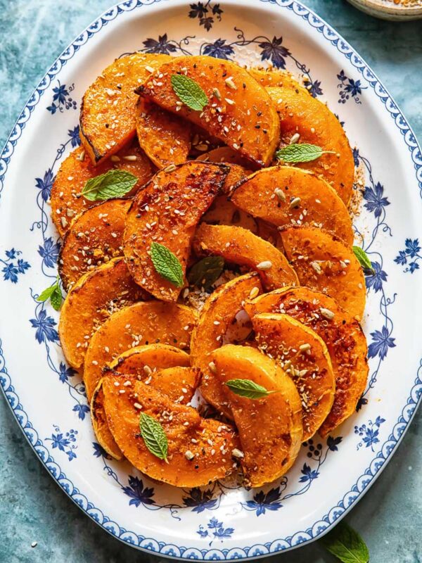roasted butternut squash slices on a plate with basil garnish