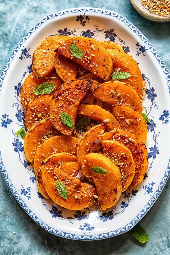 roasted butternut squash  slices on a plate with basil garnish